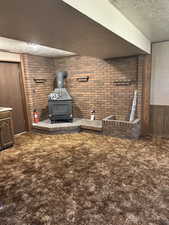 Detailed view of a wood stove, carpet, a textured ceiling, wooden walls, and brick wall