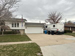Bi-level home featuring brick siding, driveway, a front yard, a large garage, and RV parking area