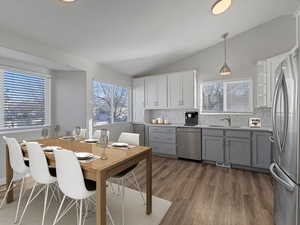 *THIS PHOTO IS VIRTUALLY STAGED TO SHOW POSSIBLE FURNITURE CONFIGURATIONS* Kitchen featuring gray cabinetry, appliances with stainless steel finishes, hanging light fixtures, lofted ceiling, and dark wood finished floors