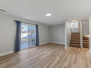 Unfurnished living room featuring healthy amount of natural light, light wood finished floors, and stairs