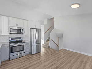 Kitchen with gray cabinetry, appliances with stainless steel finishes, white cabinets, light wood-style floors, and decorative backsplash