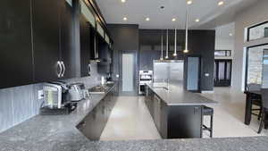 Kitchen featuring glass insert cabinets, dark cabinets, stainless steel appliances, a breakfast bar, and a large island