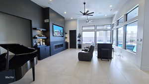 Living room with a ceiling fan, a glass covered fireplace, a towering ceiling, recessed lighting, and light tile patterned flooring