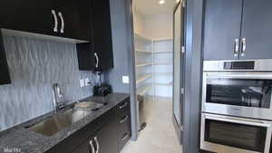 Kitchen with dark cabinets, stainless steel double oven, dark stone counters, modern cabinets, and light tile patterned flooring