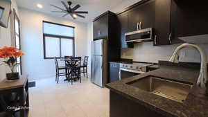 Casita kitchen with dark cabinets, stainless steel appliances, tasteful backsplash, dark stone counters, and ceiling fan