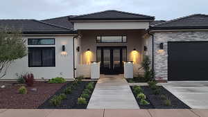 Property entrance featuring stone siding, a tiled roof, stucco siding, an attached garage, and concrete driveway