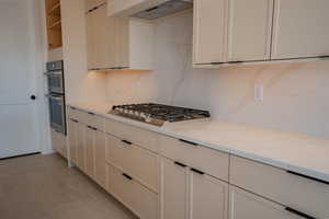 Kitchen with ventilation hood, stainless steel appliances, light stone counters, and decorative backsplash