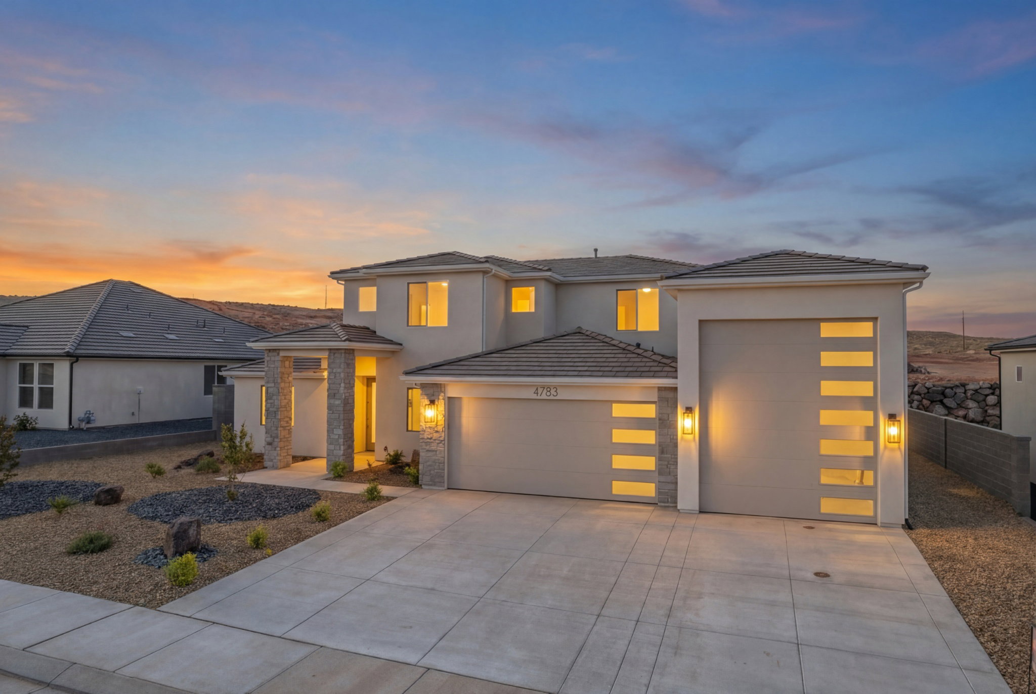 Contemporary stucco exterior featuring stone accents, a multi-paneled garage door with horizontal glass insets, an additional single-car garage, and a concrete driveway