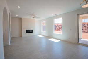 Unfurnished living room featuring a ceiling fan, a fireplace, recessed lighting, light floors, and arched walkways