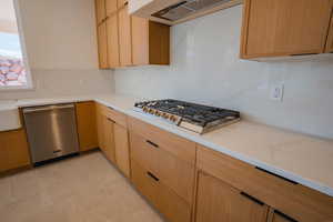 Kitchen featuring stainless steel appliances, ventilation hood, light stone counters, light brown cabinets, and modern cabinets