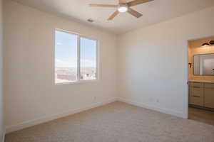 Unfurnished bedroom with light carpet, ceiling fan, and ensuite bath
