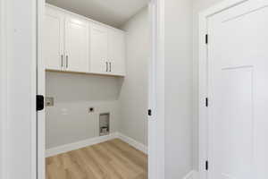 Laundry area featuring light wood finished floors, hookup for an electric dryer, and cabinet space