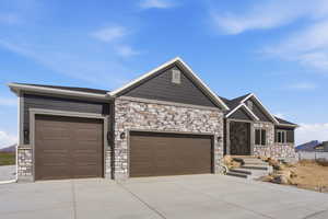 View of front of property with stone siding, an attached garage, and driveway