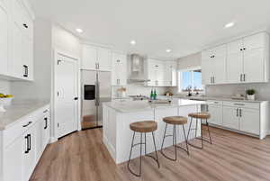 Kitchen with stainless steel fridge, white cabinetry, a center island, light wood-style flooring, and recessed lighting