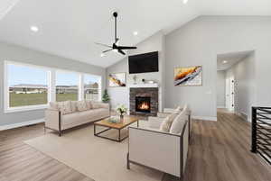 Living room with lofted ceiling, light wood-type flooring, ceiling fan, a fireplace, and recessed lighting
