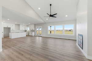 Unfurnished living room featuring light wood-style floors, ceiling fan, high vaulted ceiling, and recessed lighting
