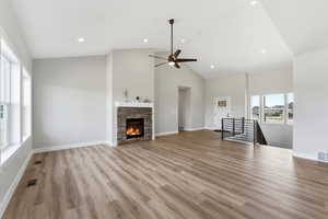 Unfurnished living room featuring light wood-type flooring, ceiling fan, a stone fireplace, lofted ceiling, and recessed lighting