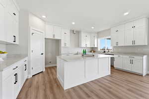 Kitchen with a kitchen island, white cabinetry, light wood-type flooring, light stone counters, and recessed lighting