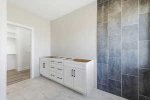 Full bath featuring double vanity, a walk in closet, and light marble finish flooring