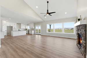 Unfurnished living room with a fireplace, vaulted ceiling, a ceiling fan, light wood-style flooring, and recessed lighting