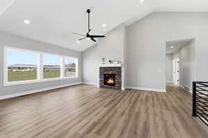 Unfurnished living room with lofted ceiling, a stone fireplace, light wood finished floors, ceiling fan, and recessed lighting