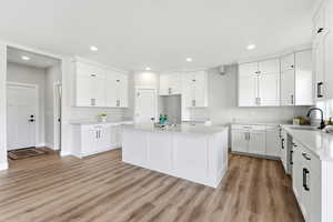 Kitchen featuring a center island, white cabinetry, light wood-style flooring, light stone countertops, and recessed lighting