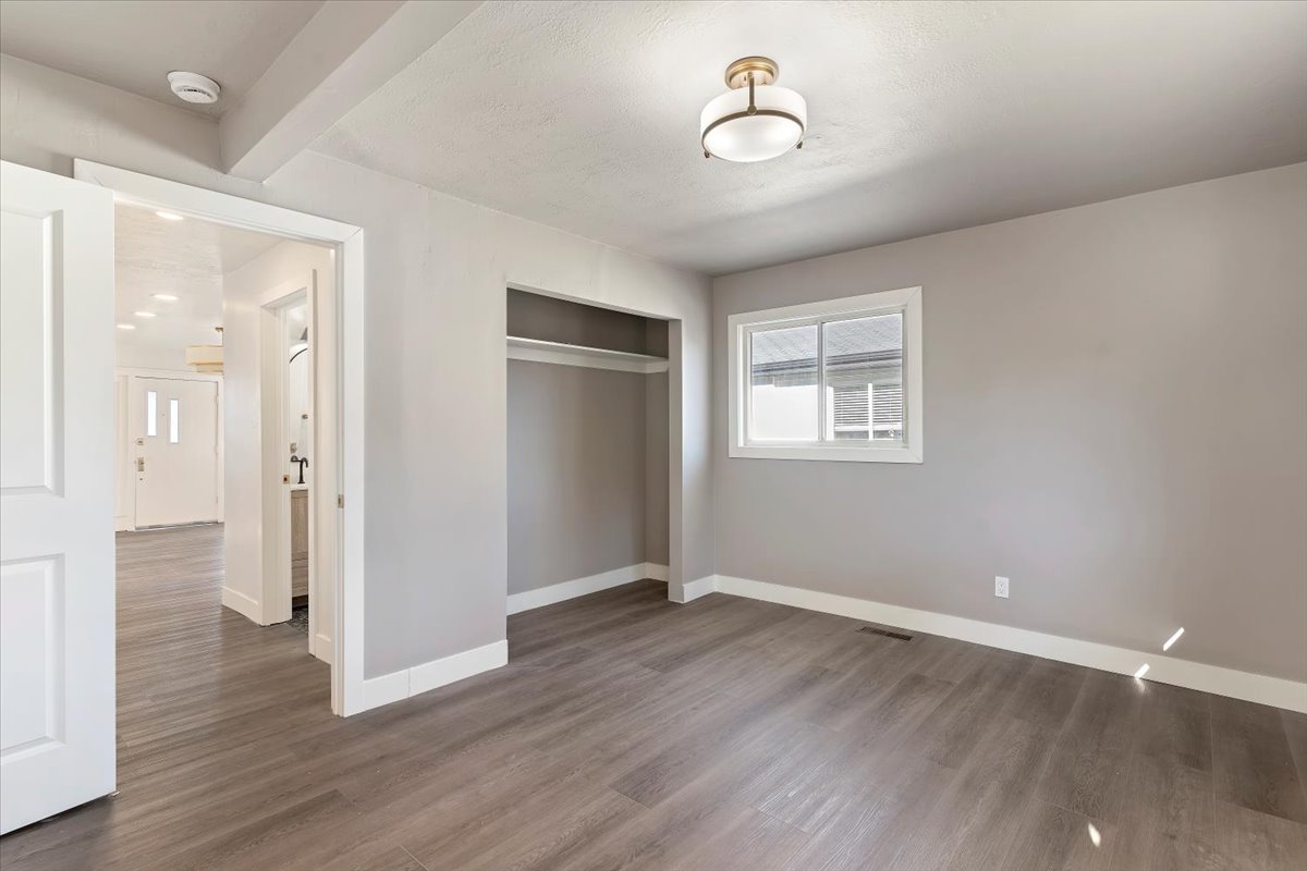Unfurnished bedroom featuring wood finished floors, a closet, and beamed ceiling