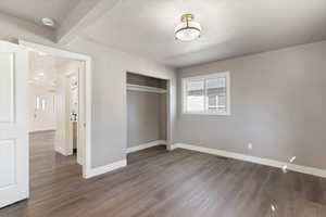 Unfurnished bedroom featuring wood finished floors, a closet, and beamed ceiling