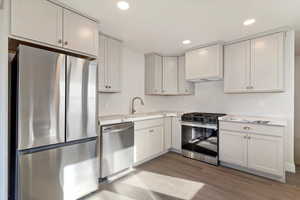 Kitchen featuring appliances with stainless steel finishes, dark wood-type flooring, recessed lighting, white cabinets, and light stone counters