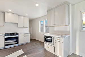 Kitchen featuring stainless steel appliances, white cabinets, recessed lighting, dark wood-style flooring, and light stone countertops