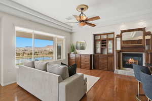 Living room with a tray ceiling, hardwood / wood-style floors, a glass covered fireplace, and a ceiling fan