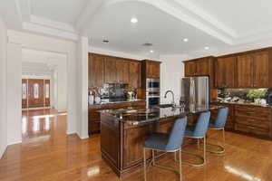 Kitchen featuring dark stone countertops, light wood-type flooring, a kitchen island with sink, a breakfast bar area, and recessed lighting
