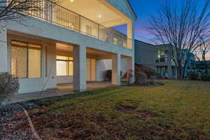 Rear view of property with a patio area, a balcony, a yard, and stucco siding