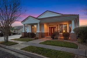 View of front of house featuring covered porch, a tile roof, stucco siding, brick siding, and a lawn