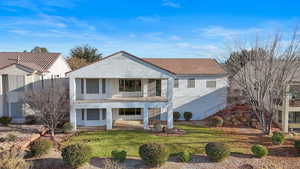 Back of house featuring a balcony, a yard, and stucco siding