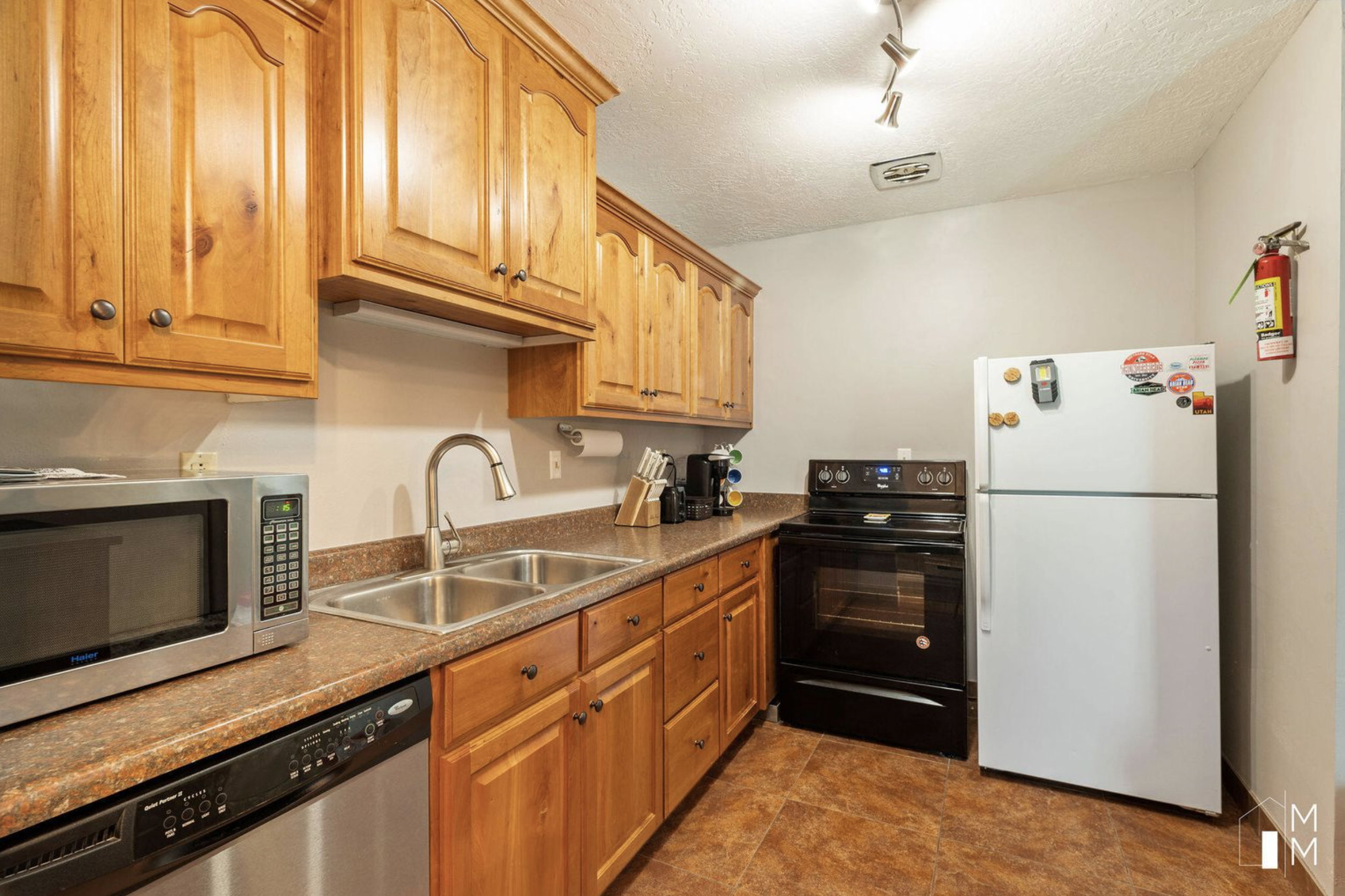 Kitchen featuring appliances with stainless steel finishes, brown cabinets, rail lighting, and a textured ceiling