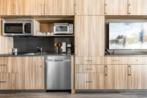 Kitchen featuring modern cabinets, light brown cabinetry, stainless steel appliances, open shelves, and backsplash
