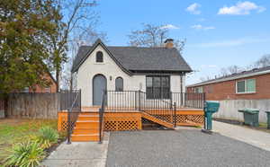 View of front of property featuring a wooden deck, a chimney, brick siding, and roof with shingles