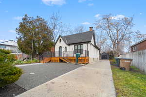 View of front of home featuring an outdoor structure, a wooden deck, a chimney, a shingled roof, and driveway