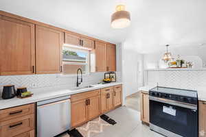Kitchen with electric range, tasteful backsplash, stainless steel dishwasher, decorative light fixtures, and light brown cabinets