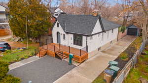 View of front facade featuring a chimney, a wooden deck, an outbuilding, and roof with shingles