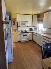 Kitchen with white cabinetry, a textured ceiling, white appliances, backsplash, and light countertops