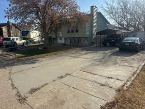 View of side of home featuring driveway, a chimney, and a lawn