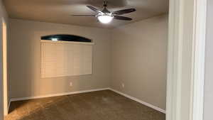 Empty room featuring dark colored carpet and a ceiling fan