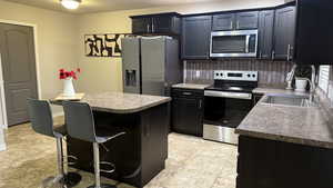 Kitchen featuring stainless steel appliances, a breakfast bar, a center island, dark countertops, and dark cabinets