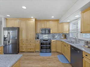 Kitchen featuring stainless steel appliances, light brown cabinetry, light stone countertops, recessed lighting, and light wood-type flooring