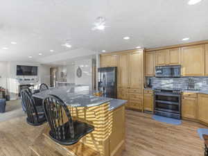 Kitchen with a breakfast bar, stainless steel appliances, dark stone counters, open floor plan, and light wood finished floors