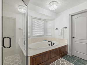 Bathroom with a textured ceiling, a shower stall, a chandelier, a jetted tub, and dark tile patterned floors