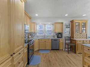 Kitchen featuring appliances with stainless steel finishes, light stone counters, glass insert cabinets, light wood-type flooring, and a textured ceiling