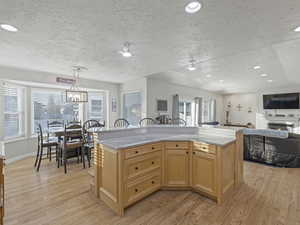 Kitchen with light brown cabinetry, a textured ceiling, light stone counters, recessed lighting, and an island with sink